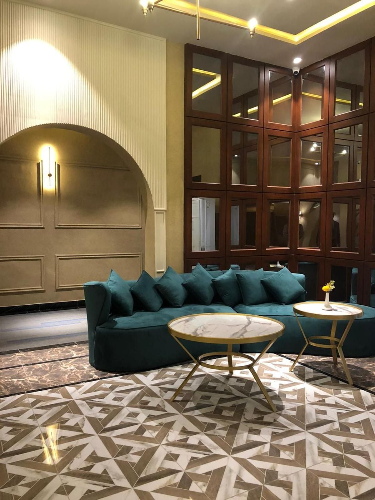 A room with a green sofa, two round tables, patterned flooring, and a large wooden cabinet with glass doors.