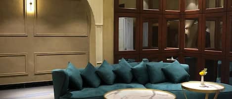 A room with a green sofa, two round tables, patterned flooring, and a large wooden cabinet with glass doors.