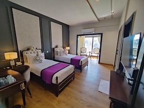 A hotel room with two beds, a desk with a lamp, a chair, and a television.