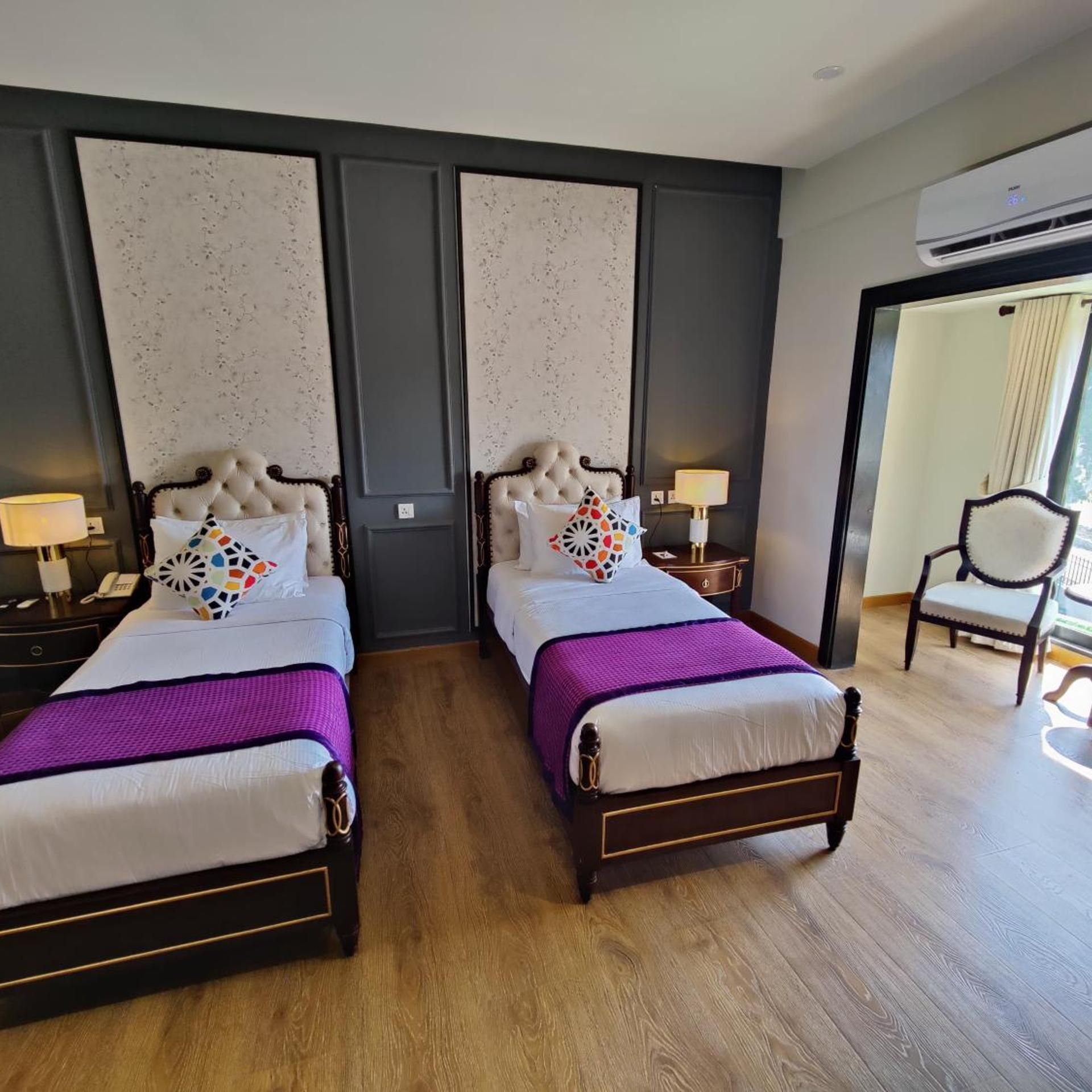 Une chambre d’hôtel avec deux lits, un plancher en bois, un mur de couleur sombre et un appareil de climatisation.