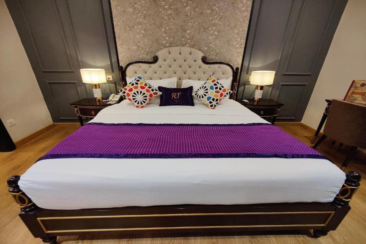 A large bed with a tufted headboard, two bedside tables with lamps, and a decorative wall panel behind the bed.