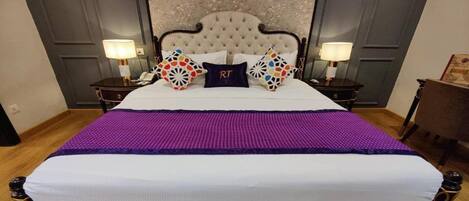 A large bed with a tufted headboard, two bedside tables with lamps, and a decorative wall panel behind the bed.