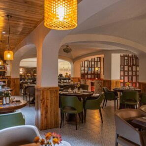 L’intérieur d’un restaurant avec des poutres en bois, des chaises vertes et des tables dressées pour le service.