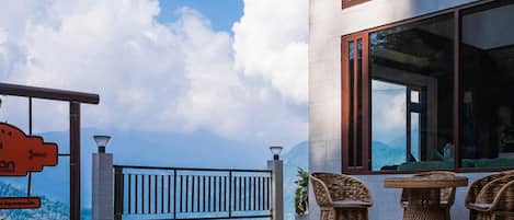 Un edificio moderno con amplios ventanales, un balcón con muebles de mimbre y vistas al cielo y las nubes.