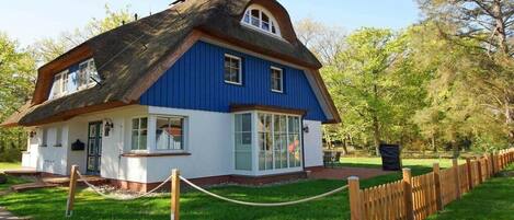 A traditional house with a thatched roof, white walls, and a blue exterior.