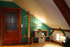 Ein Zimmer mit Holztür, einer Wand in Grün-kariert, einem Holzregal mit Körben und einer Lampe.