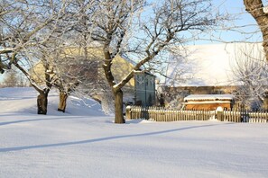 Schneebedeckte Landschaft mit kahlen Bäumen und einem Gebäude mit verschneitem Dach.