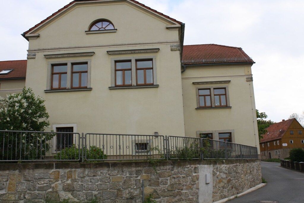 A two-story building with a stone facade, multiple windows, and a metal fence.