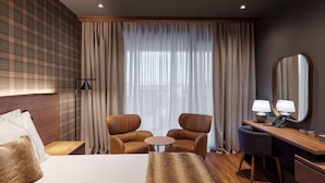 Une chambre d’hôtel comprenant un lit, deux fauteuils, une petite table, un bureau avec une lampe, un téléphone et un grand miroir.