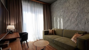 Una habitación moderna con un escritorio de madera, un sofá verde, una mesa de centro redonda y una lámpara.
