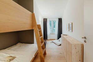 Ein Schlafzimmer mit Etagenbetten, einer Holzleiter, einem Fenster mit Vorhängen und einer Tür zu einem weiteren Raum.