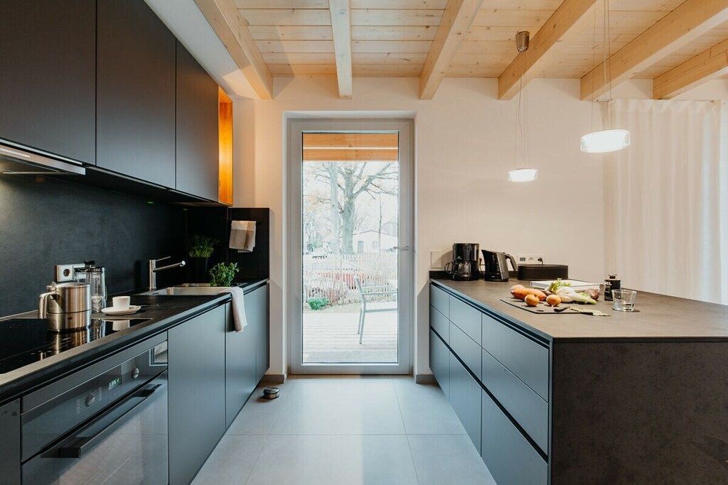 A modern kitchen with dark cabinetry, a built-in oven, and a large island with a coffee maker and food items.