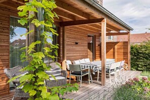 Eine Holzhütte mit überdachter Terrasse, ausgestattet mit Korbmöbeln und einem Tisch.