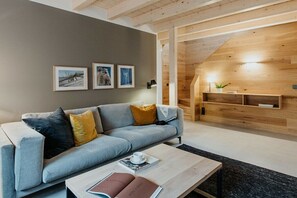 Ein modernes Wohnzimmer mit einem grauen Sofa, einem Couchtisch mit Büchern und einer Holzwand mit schrägverlaufender Decke.