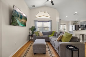 A modern living room with a gray sofa, a coffee table, and a large window with curtains. - Tivoli Manor Retreat | Cozy Florida Getaway (Davenport)