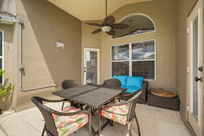 An outdoor patio with a table and chairs, a ceiling fan, and a window with blinds. - Tivoli Manor Retreat | Cozy Florida Getaway (Davenport)
