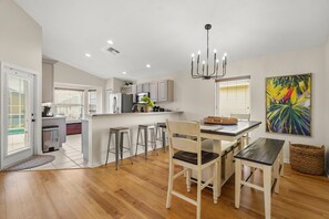 A modern kitchen with a dining area, wooden flooring, and a large window. - Tivoli Manor Retreat | Cozy Florida Getaway (Davenport)