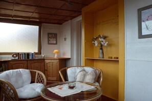 A room with wicker chairs, a round glass table, a bookshelf, and a wall with a decorative vase. - Holiday home Elbe Sandstone Mountains (Königstein)