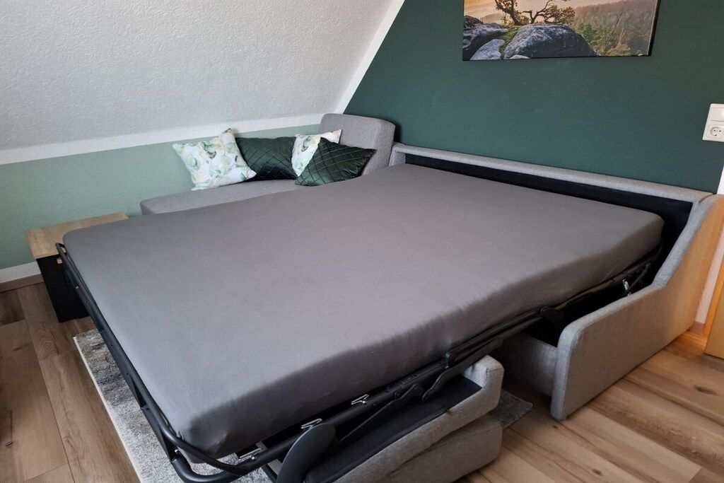 A bed with a grey mattress and a pull-out drawer underneath.