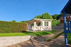 A small white playhouse with a roof and windows, surrounded by a brick wall and a green hedge. - Holiday home Elbe Sandstone Mountains (Königstein)
