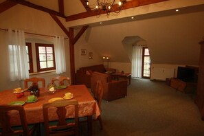 A dining area with a table set for four, a sofa, and a television in a room with sloped ceilings and wooden beams. - Holiday apartment with 2 bedrooms (Bahretal)