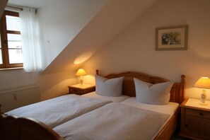 A bedroom with two beds, wooden headboards, bedside tables with lamps, a radiator, and a window with curtains. - Holiday apartment with 2 bedrooms (Bahretal)