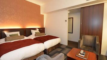 A hotel room with two beds, a small table, a chair, and a wooden wardrobe.