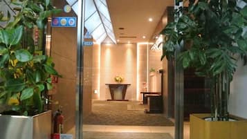 A hotel lobby with a reception desk, a fireplace, and potted plants.