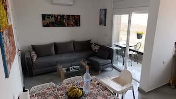 Un salon comprenant un canapé, une table basse, une table à manger avec des chaises et une porte-fenêtre coulissante donnant sur un espace extérieur.