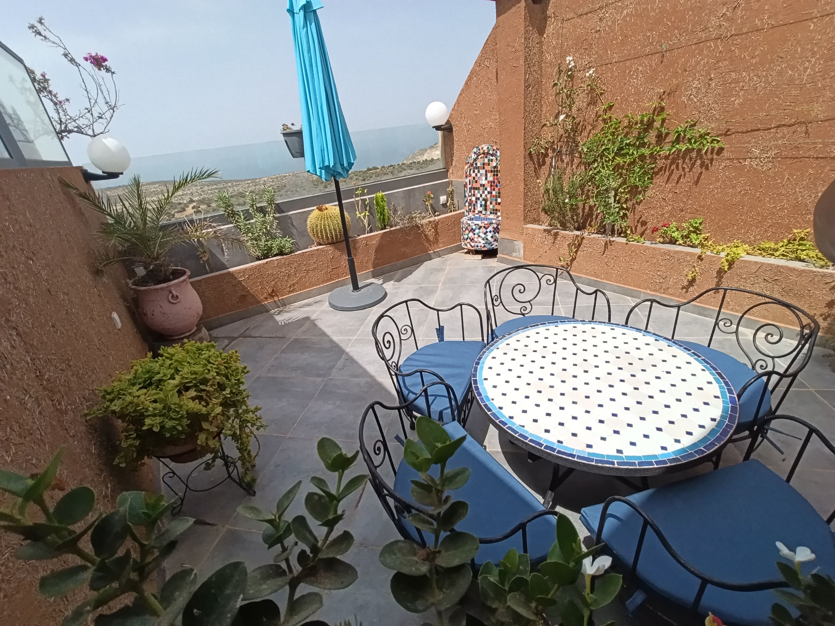 Une terrasse avec une table ronde et des chaises, entourée de plantes en pot et offrant une vue sur le paysage.
