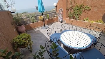 Une terrasse avec une table ronde et des chaises, entourée de plantes en pot et offrant une vue sur le paysage.