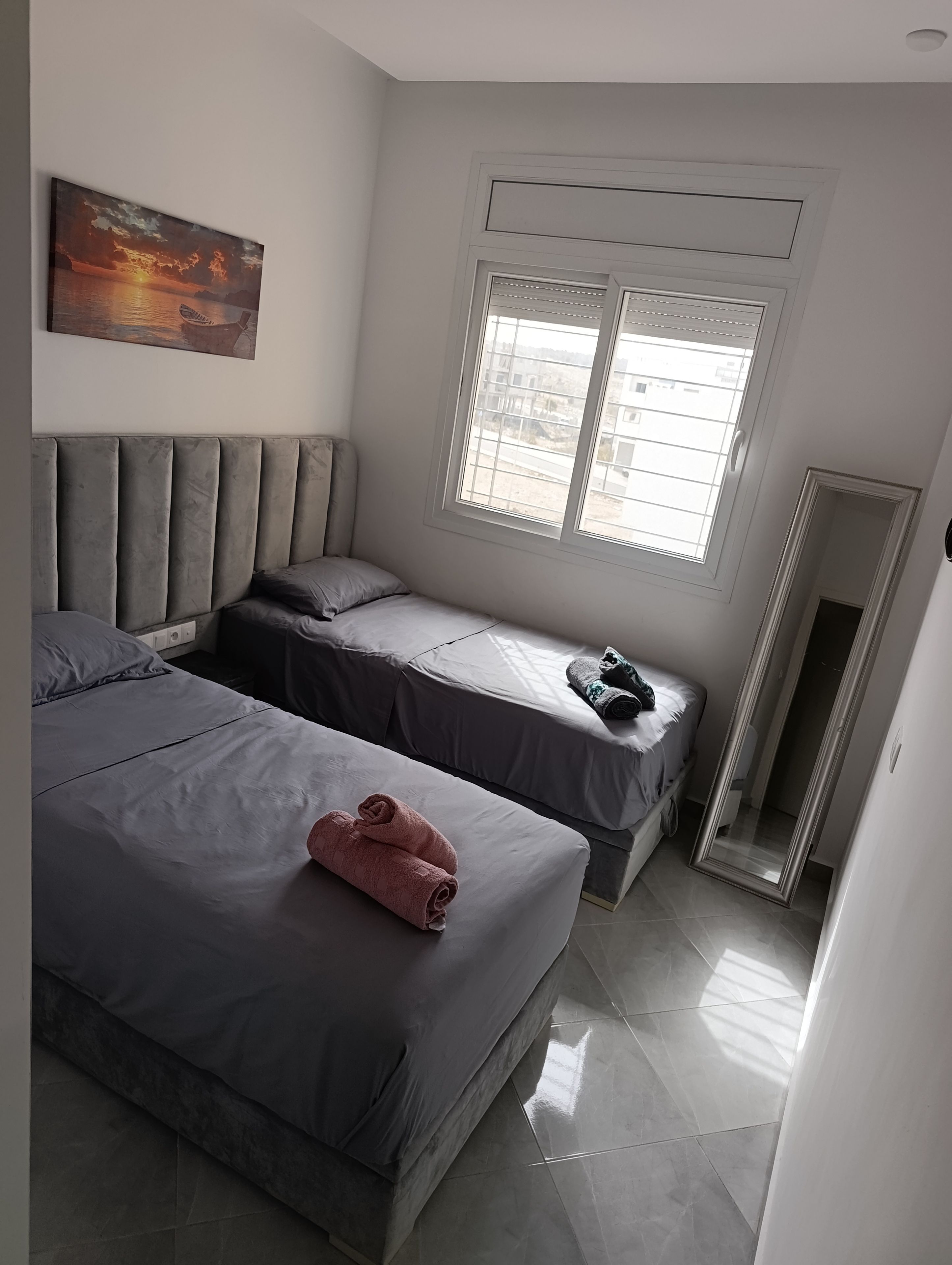 Une chambre avec deux lits, une grande fenêtre et un tableau au mur.