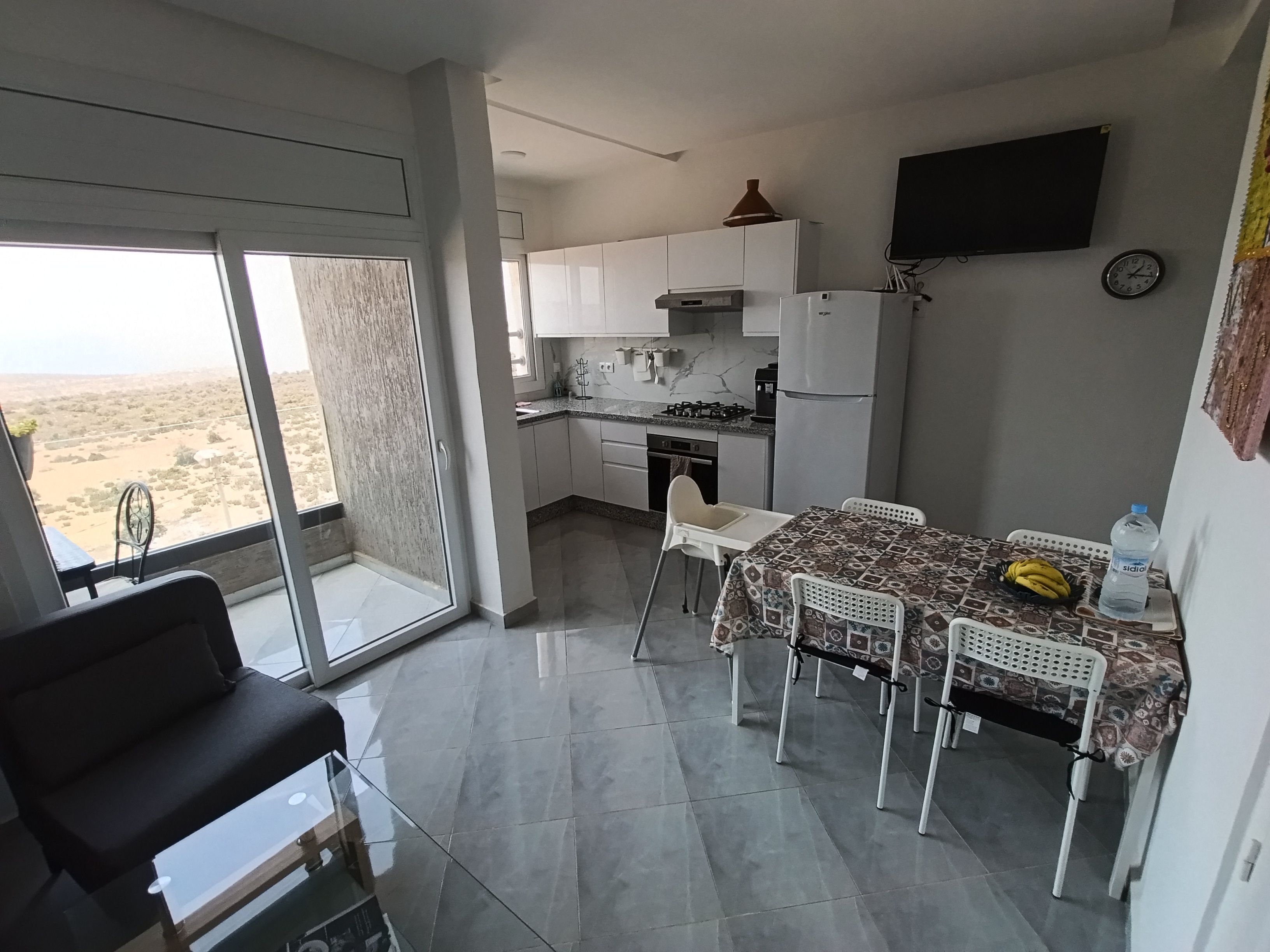 A modern kitchen with white cabinets, a dining table with chairs, and a large window overlooking a desert landscape.