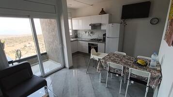 Une cuisine moderne avec des meubles blancs, une table à manger avec des chaises et une grande fenêtre donnant sur un paysage désertique.