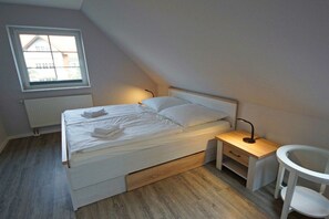 Ein Schlafzimmer mit Bett, Nachttisch, Lampe und einem kleinen weißen Stuhl.