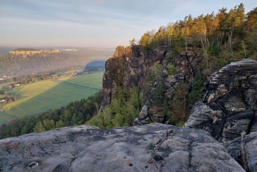 A rocky cliff overlooking a valley with fields and a distant town.