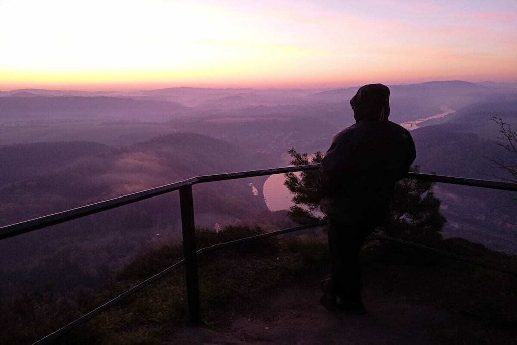 A person standing at a railing overlooking a valley during sunset.