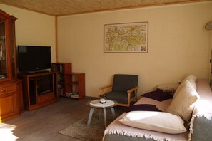 Un saló amb televisió, un mapa a la paret, un sofà i una cadira.