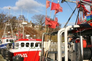 Un vaixell vermell i blanc anomenat Emilia amarrat a un port amb altres embarcacions, un edifici al fons i un cel serè.