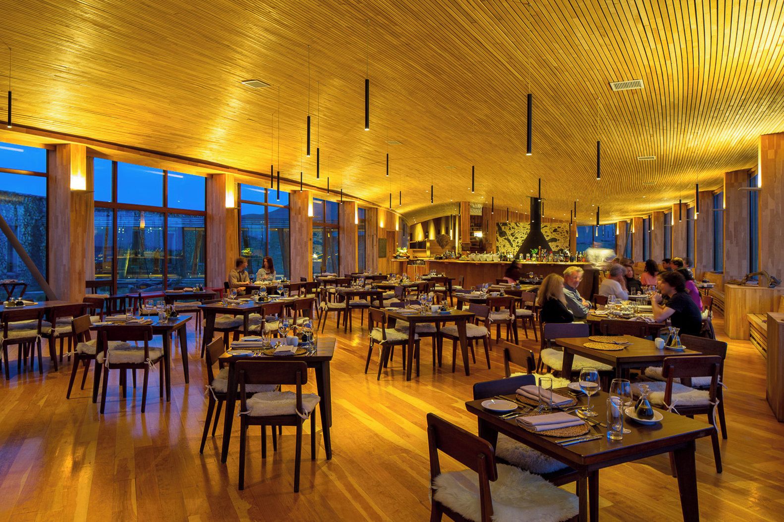 Un restaurante espacioso con suelo de madera, mesas, ventanas amplias y un techo alto con vigas de madera.