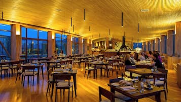 Un restaurante espacioso con suelo de madera, mesas, ventanas amplias y un techo alto con vigas de madera.