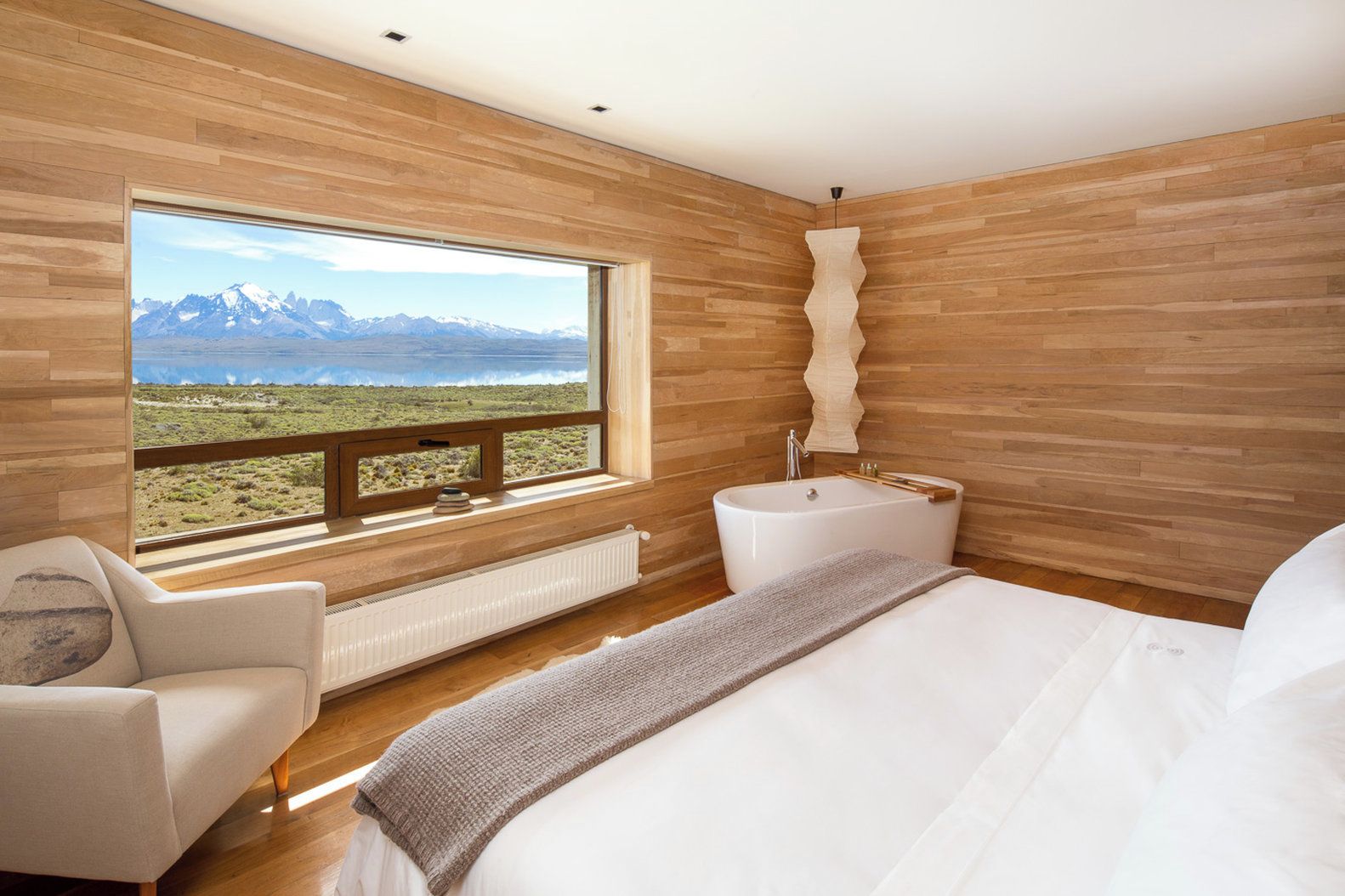A bedroom with a large window, a bathtub, and a view of mountains.