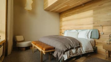 Un dormitorio con cama, banco, mesita de noche y lámpara de pared.
