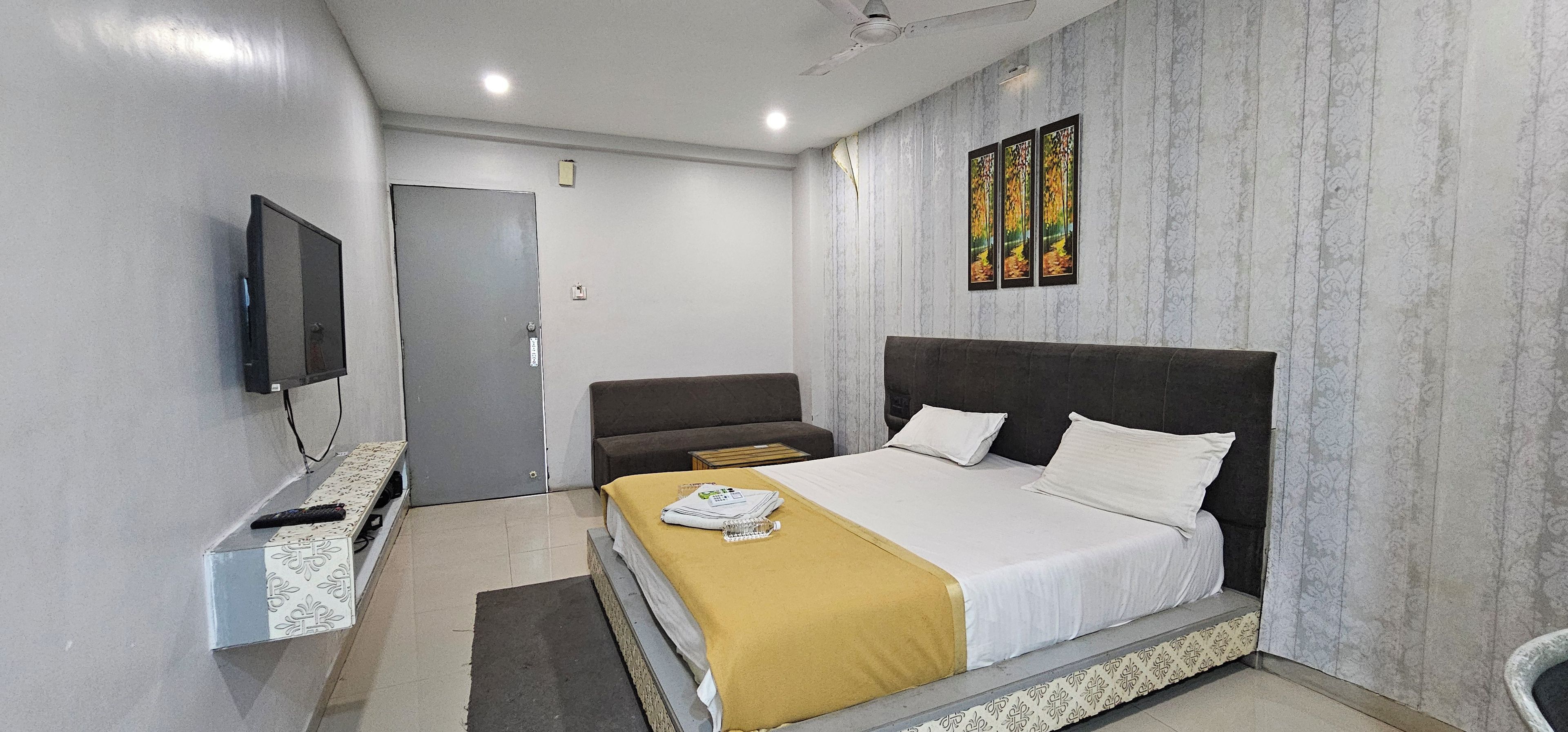A hotel room with a bed, a sofa, a television, and a painting on the wall.