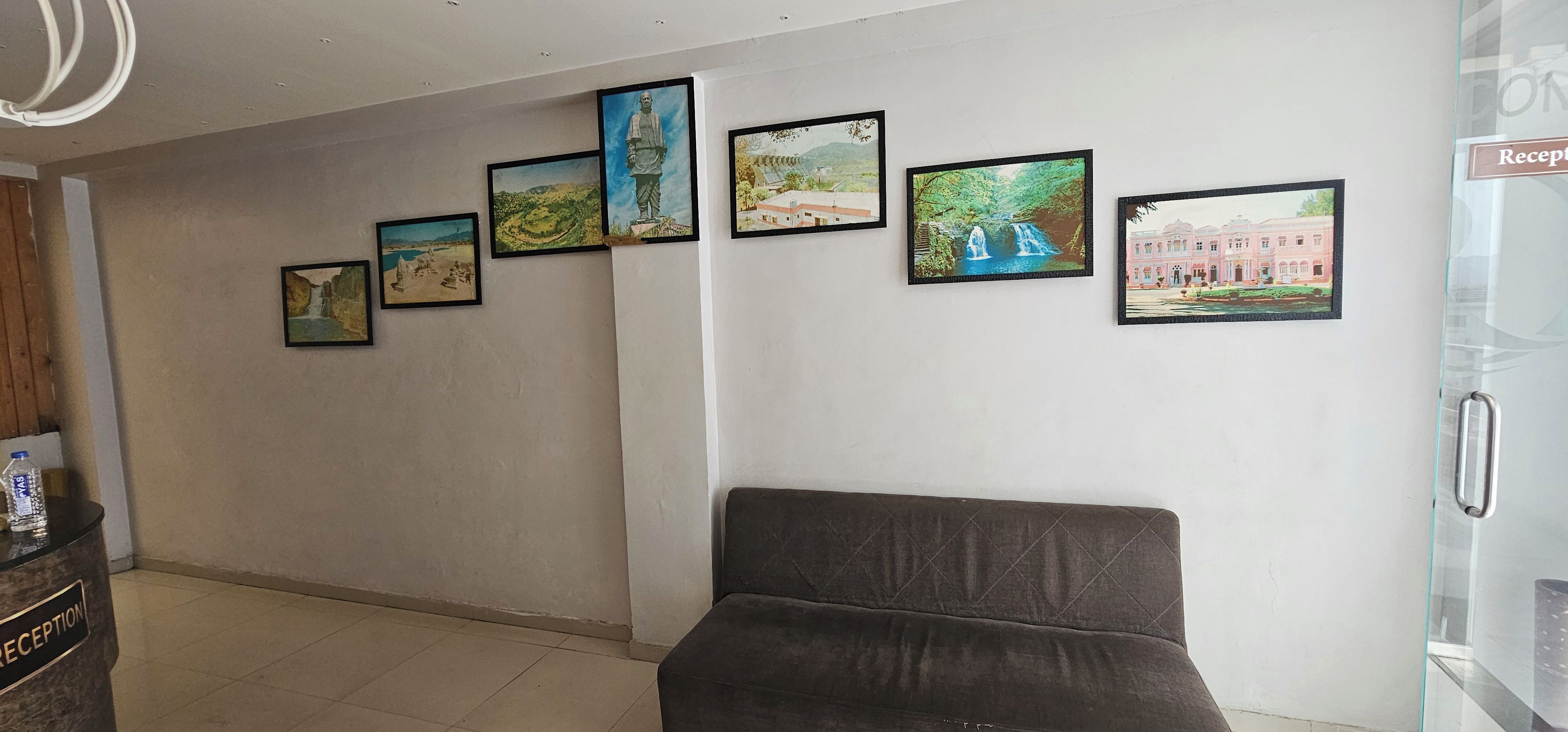 Un área de recepción con un sofá, dispensador de agua y una pared con fotografías enmarcadas.