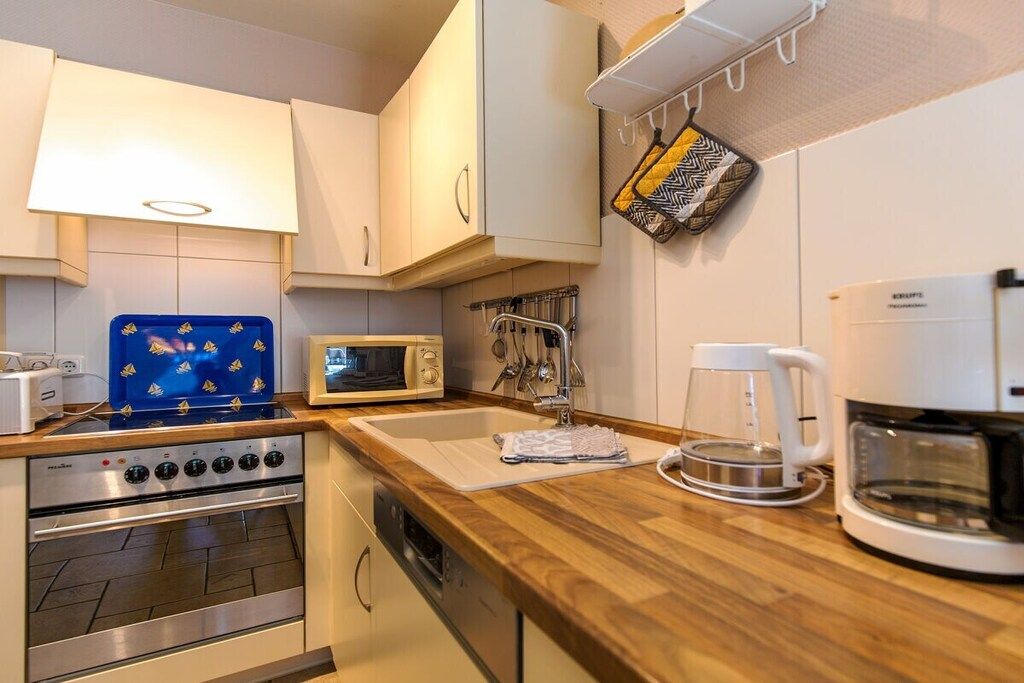 A compact kitchen with a microwave, stove, coffee maker, and hanging utensils.
