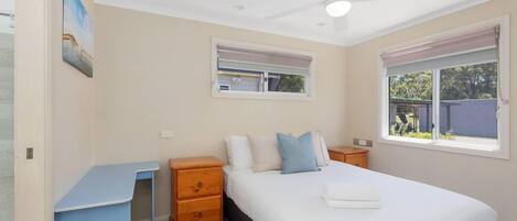 Un dormitorio con cama, escritorio, ventilador de techo y ventana.