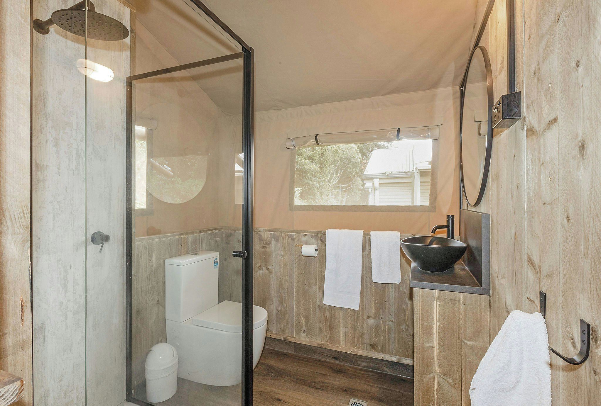 A bathroom with a glass shower enclosure, a toilet, a sink with a basin, and a window providing natural light.