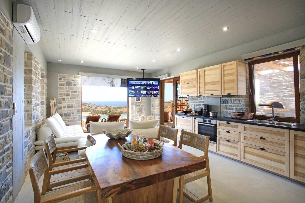 A modern kitchen with wooden cabinets, a dining area with a wooden table and chairs, and a large TV screen.