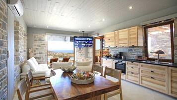 A modern kitchen with wooden cabinets, a dining area with a wooden table and chairs, and a large TV screen.